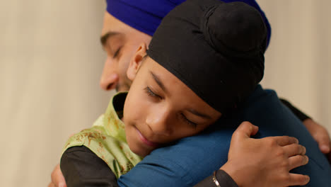 Close-Up-Studio-Shot-Of-Sikh-Father-Embracing-Son-Both-Wearing-Turbans-Against-Plain-Background-2